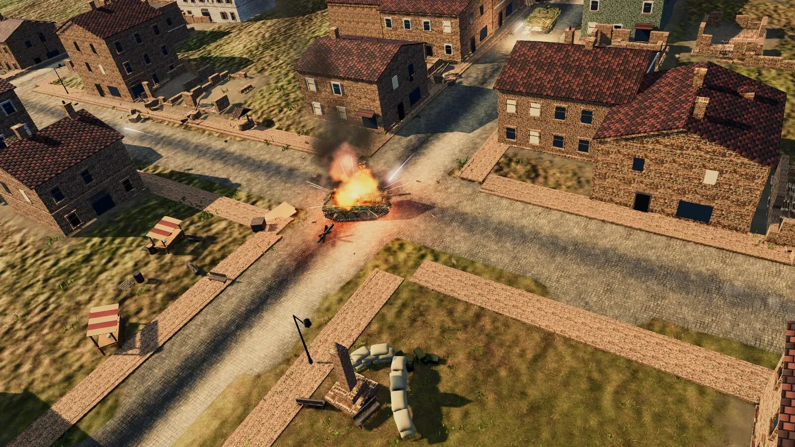 A tank burns at a crossroads in a brick village, seen from above